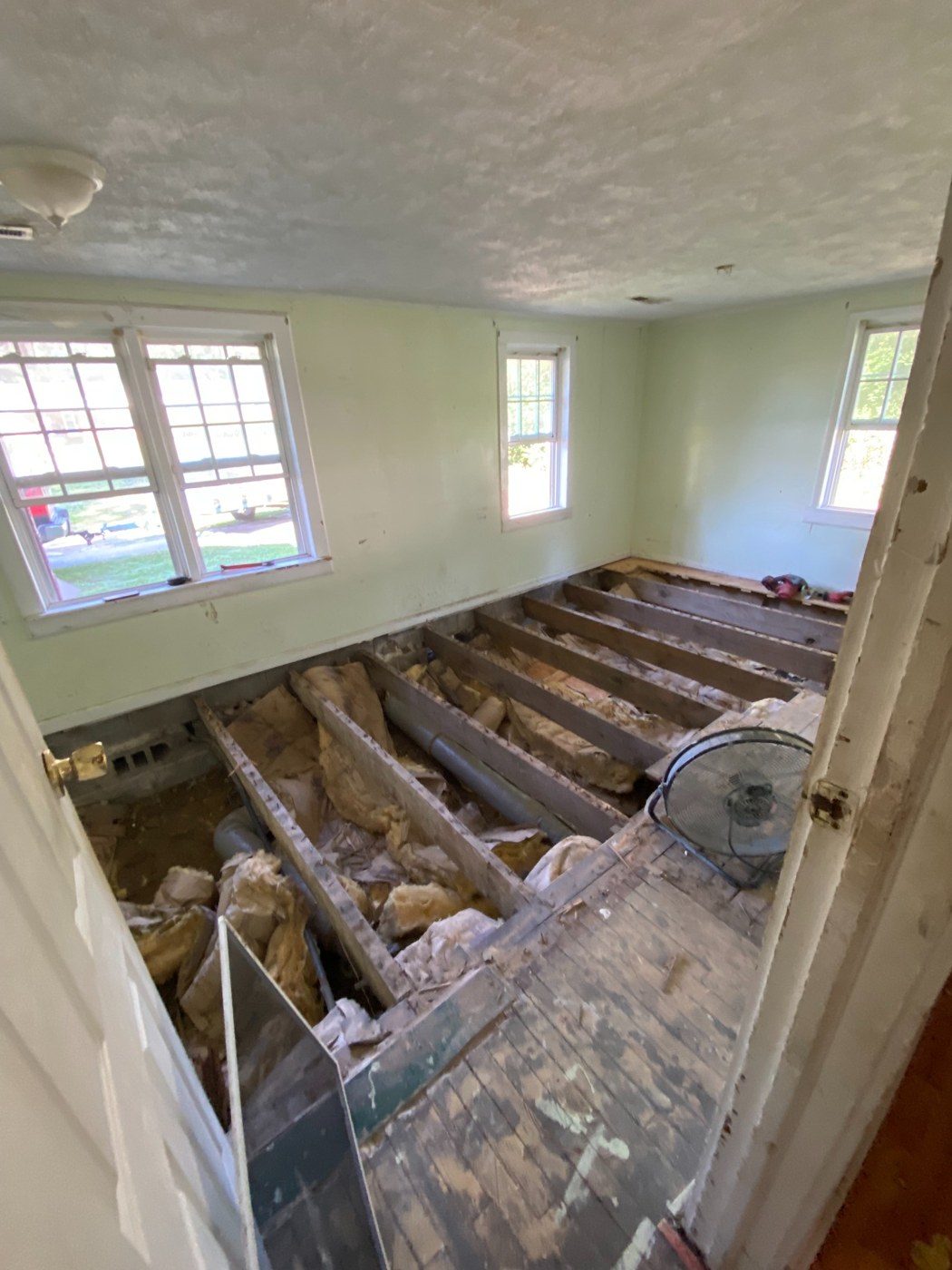 Room with old flooring removed and existing joists and insulation exposed.