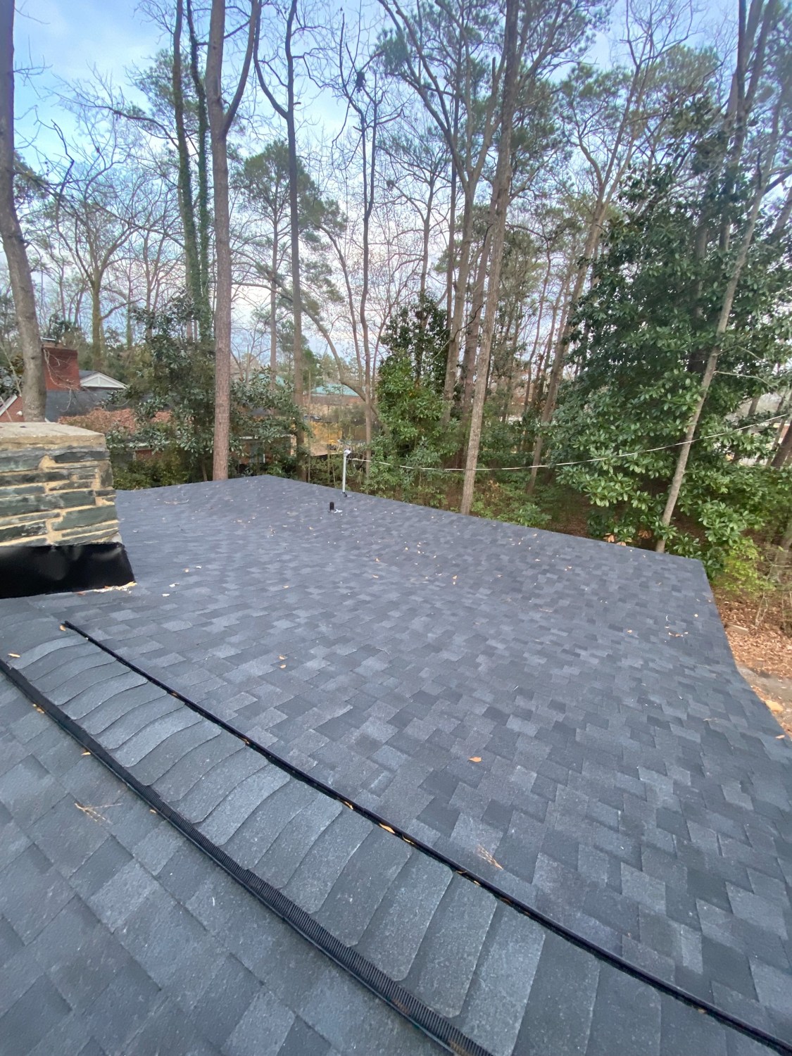 New gray shingles installed on the same roof beside the stone chimney.